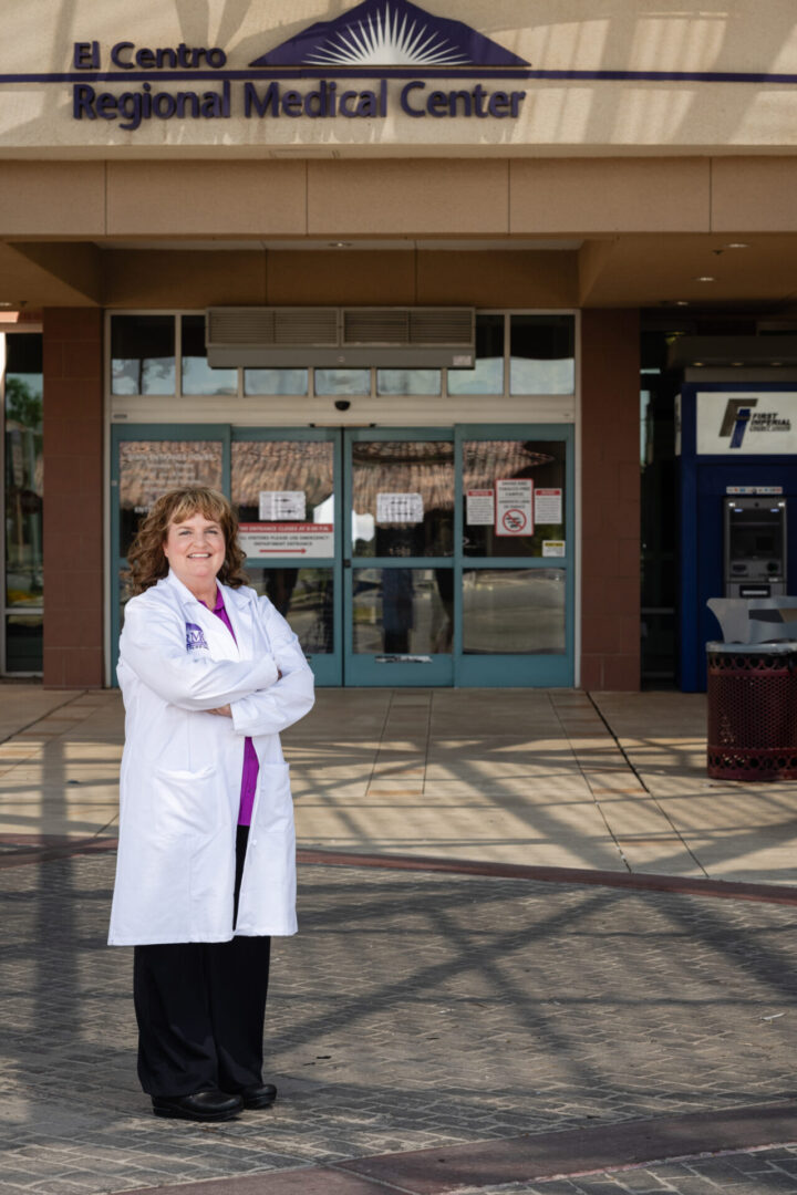 A woman in white lab coat standing outside of building.