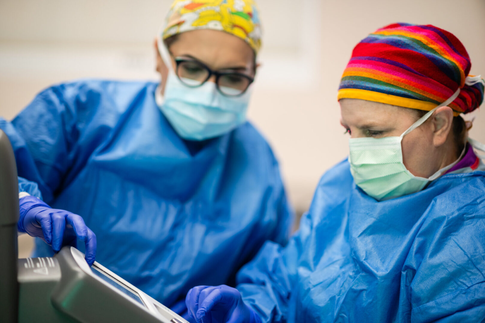 Two doctors in blue scrubs and masks looking at a laptop.